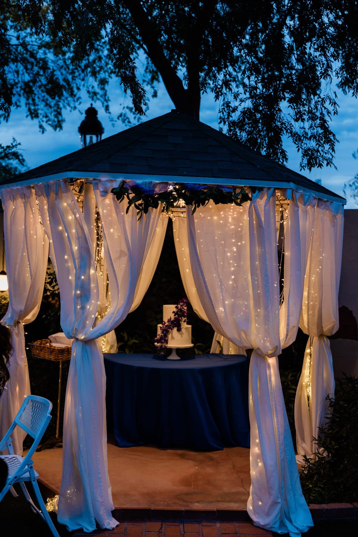 The draped ceremony structure glowing at dusk, with the wedding cake inside.